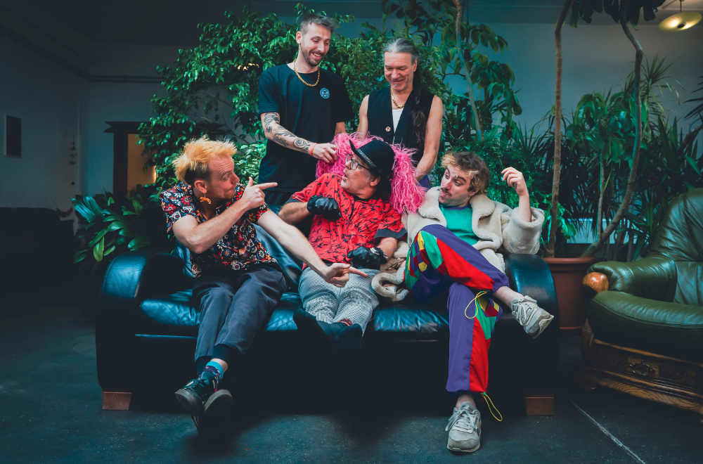 Die Band Malaka Hostel sitzt in bunter Kleidung auf einem Sofa