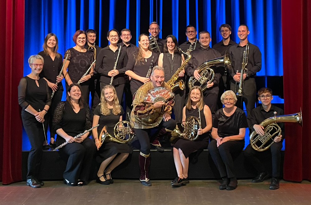 Bernd Lafrenz steht umgeben von Musikerinnen und Musikern des Riegelers Musikverein vor einem blauen Theatervorhang.